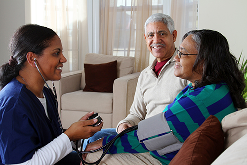 Nurse sitting in front of a couple sitting on a couch and taking the wife's blood pressure